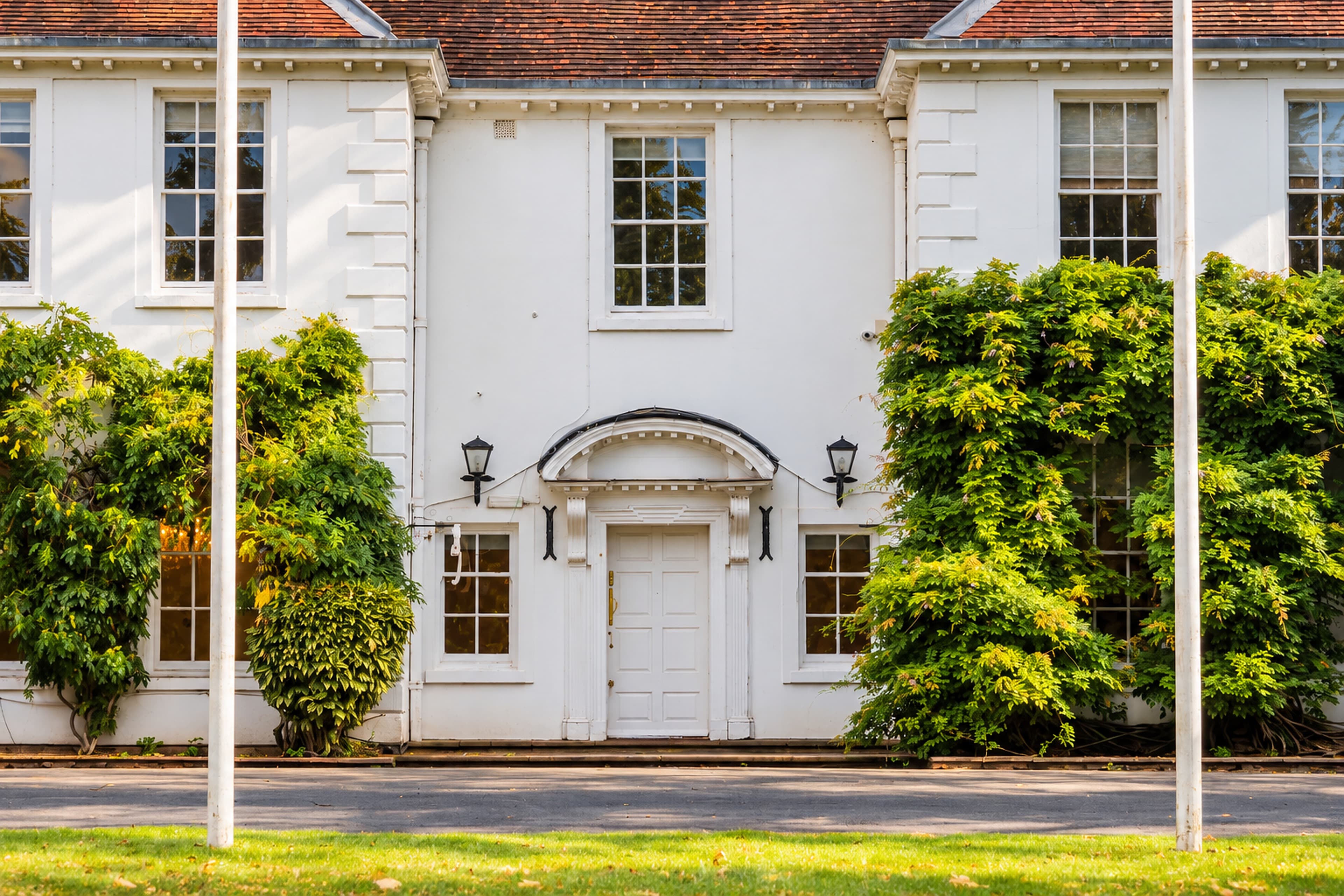 A close-up of Longbridge Manor’s white front door and arched canopy, with wall lanterns and climbing greenery on either side