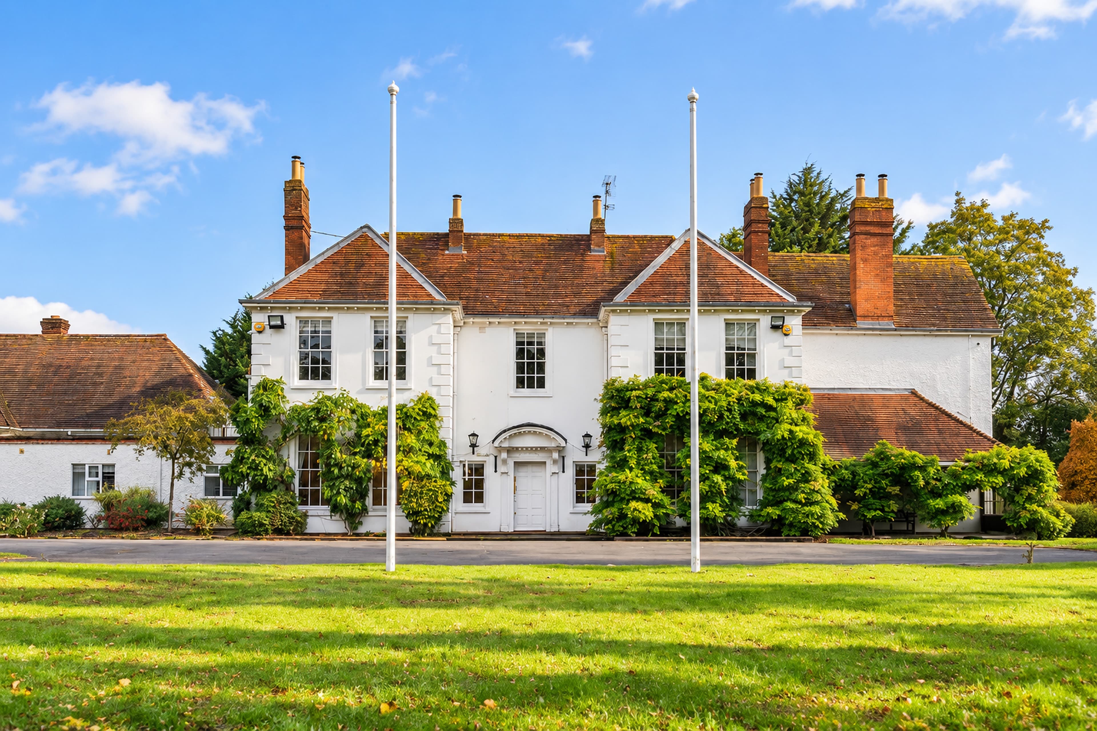 A wide, symmetrical view of Longbridge Manor and both wings, with two flagpoles and the front lawn beneath a blue sky
