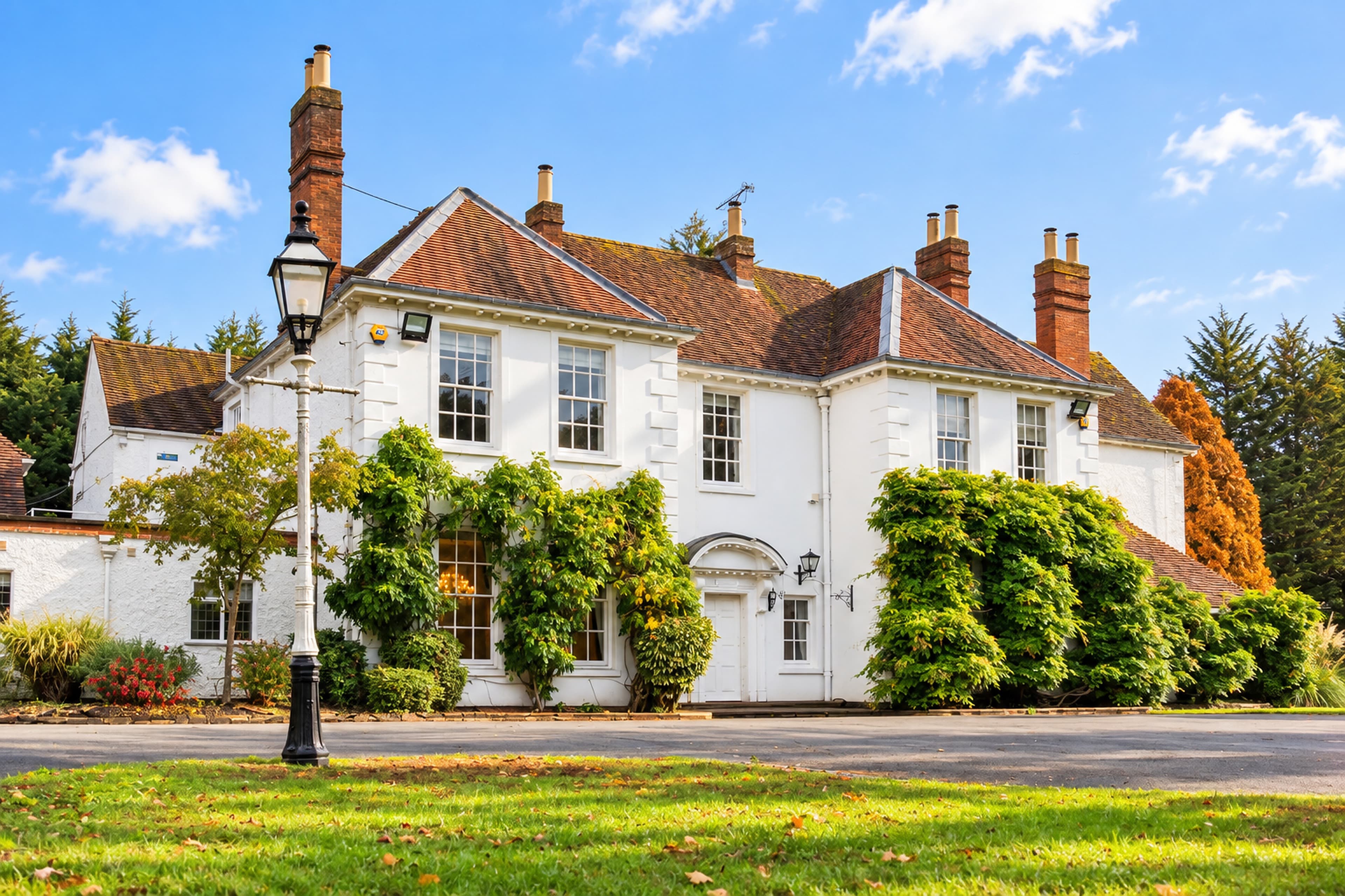 Longbridge Manor from the left, with its white façade and climbing plants behind a tall courtyard lantern and sunlit grass