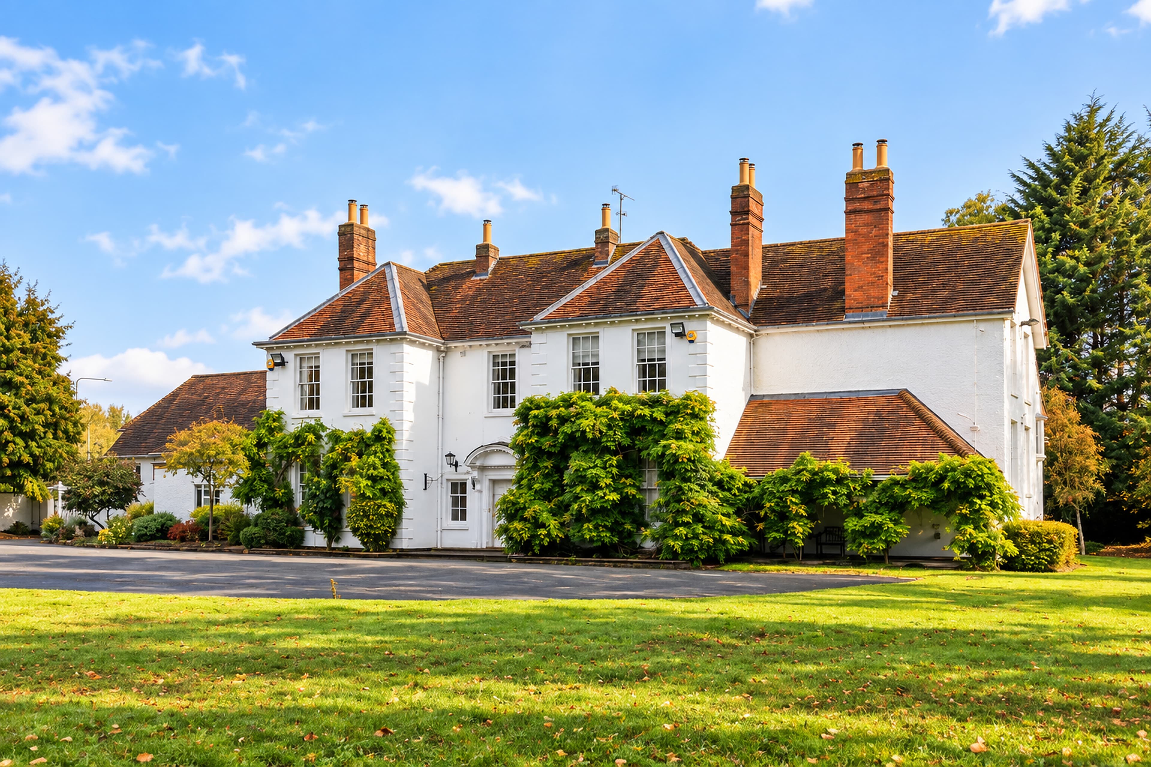 A wide view of Longbridge Manor from the right, showing its white walls, red-tiled roofs, brick chimneys and surrounding lawn