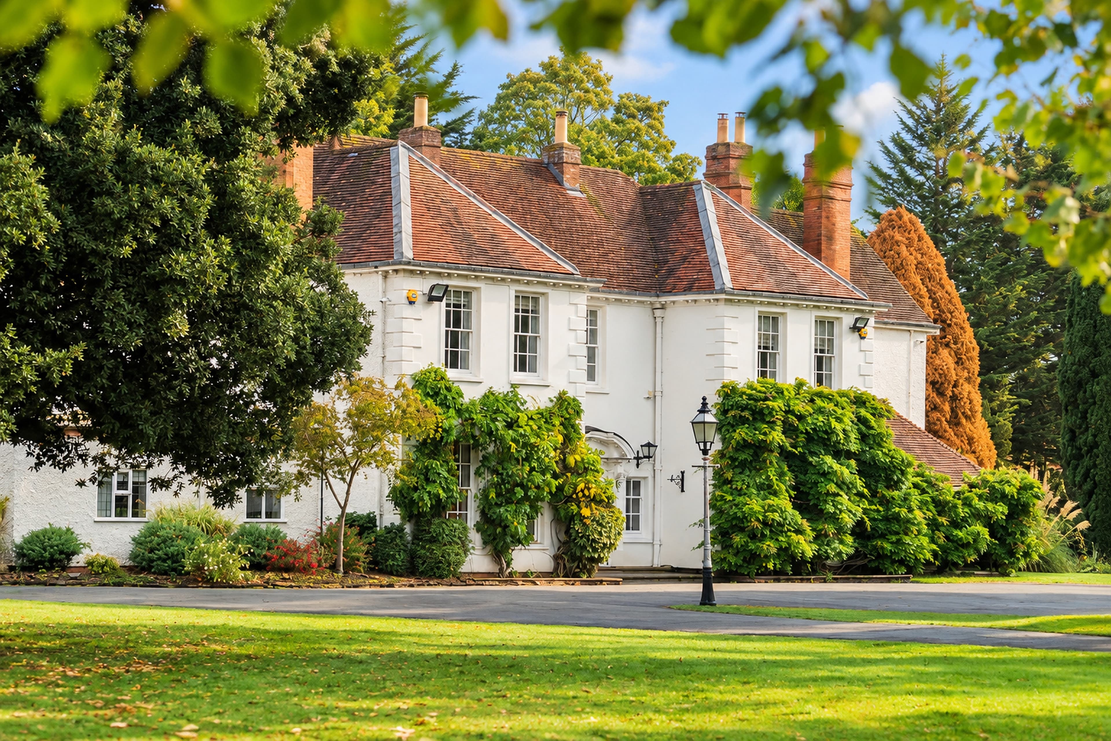 Longbridge Manor’s white façade and red-tiled roof, framed by mature trees and sunlit lawns